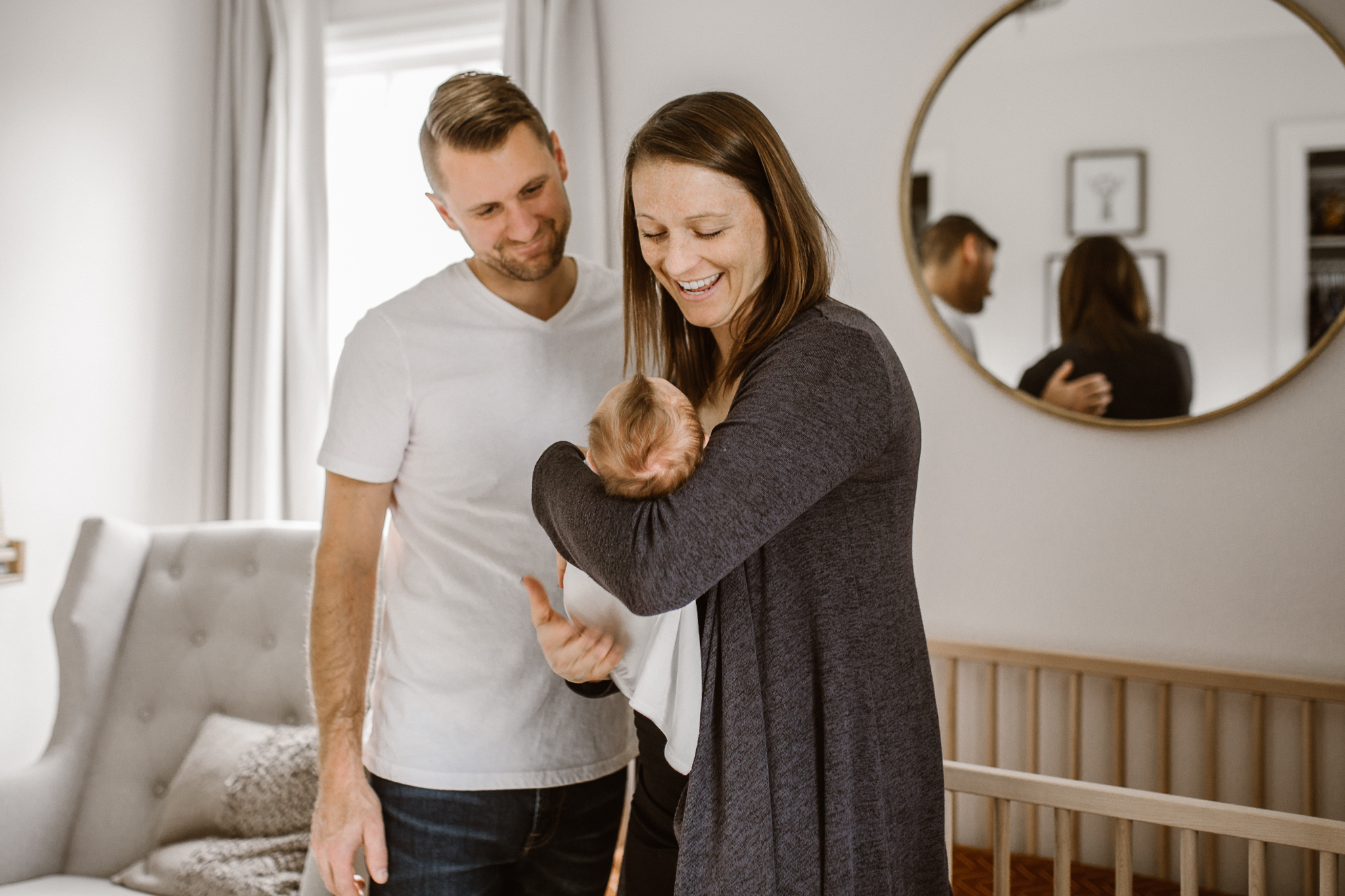 New parents in the nursery holding their baby as dad's hand rests on mom's back.